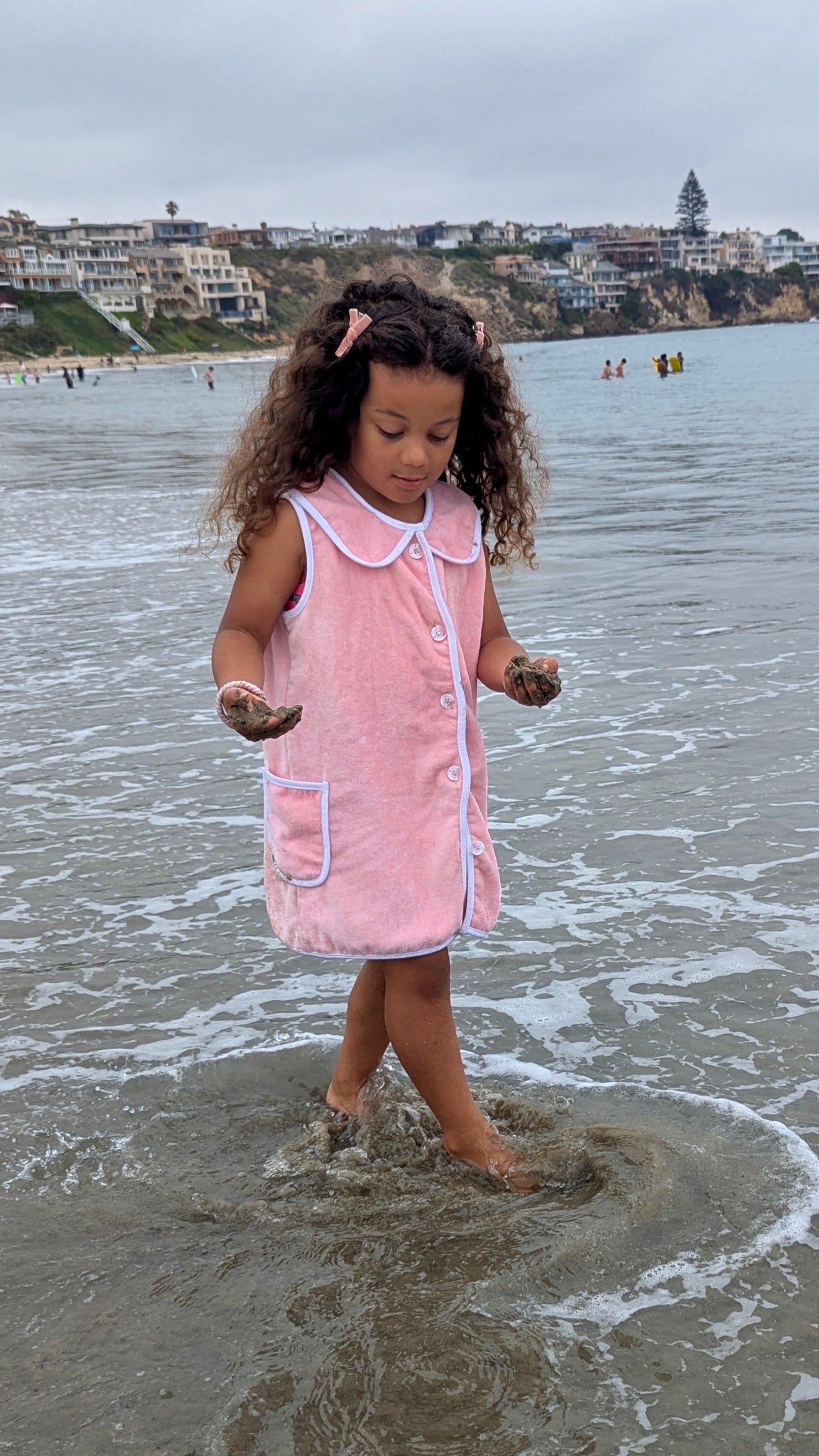 Young girl in a pink dress playing in the water at the beach.